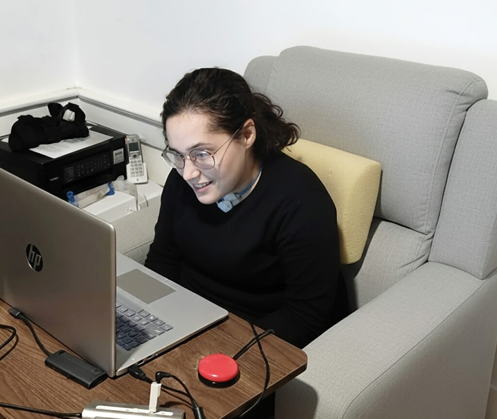 Esther, seated in a recliner facing her laptop