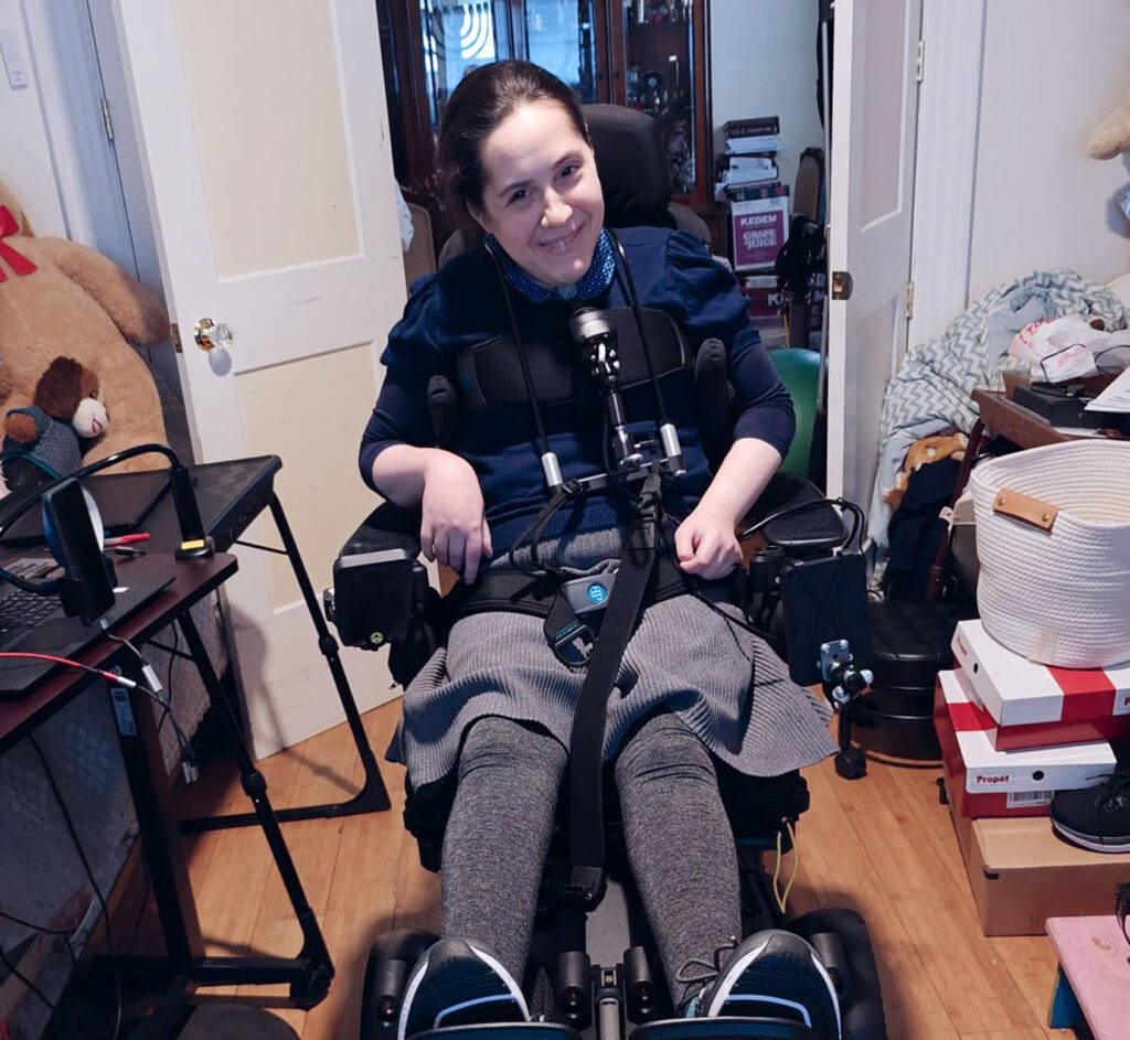 Esther sitting in a motorized wheelchair with a smile on her face.